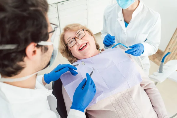 Squadra di dentisti che parlano con il paziente anziano durante l'intervento — Foto Stock