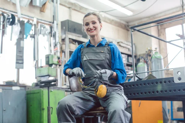 Mechanikerin sitzt in Metallwerkstatt und blickt in Kamera — Stockfoto