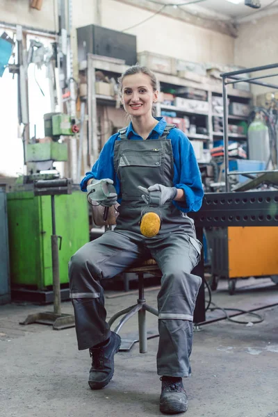 Mechanikerin sitzt in Metallwerkstatt und blickt in Kamera — Stockfoto