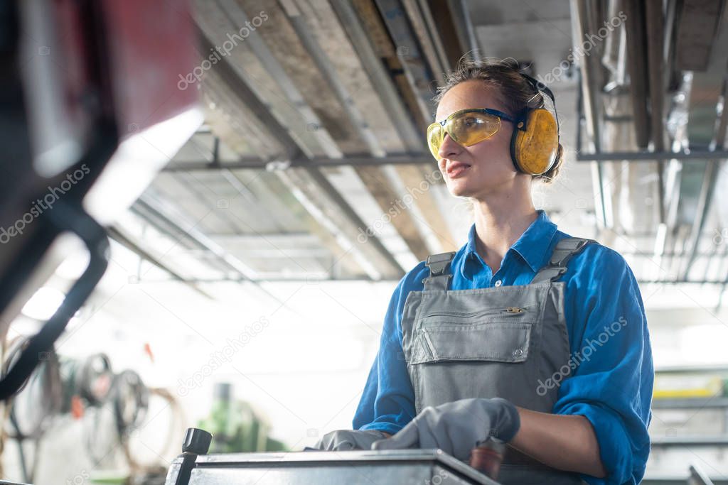 Woman worker operating a machine tool in metal workshop or facto