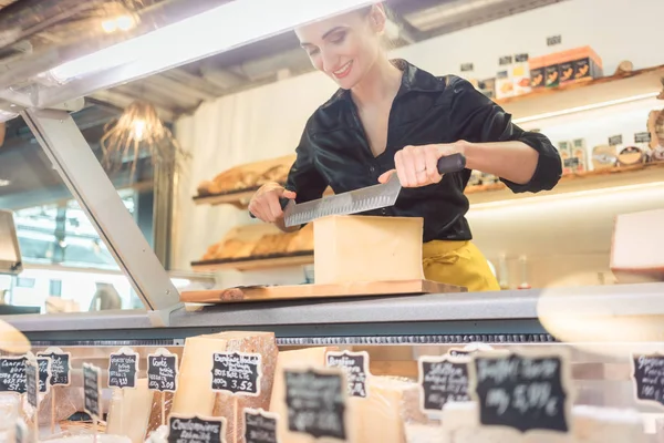 Jeune vendeuse en charcuterie coupant du fromage — Photo