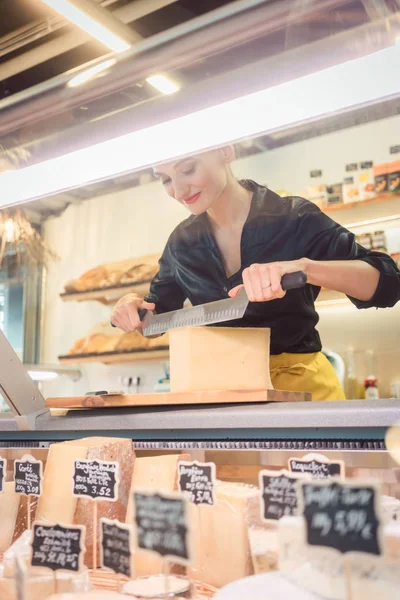 Junge Verkäuferin im Feinkostladen schneidet Käse — Stockfoto