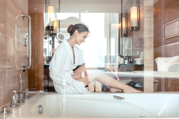 Vrouw verwijderen van haren door het scheren van haar benen in de badkamer van het hotel — Stockfoto