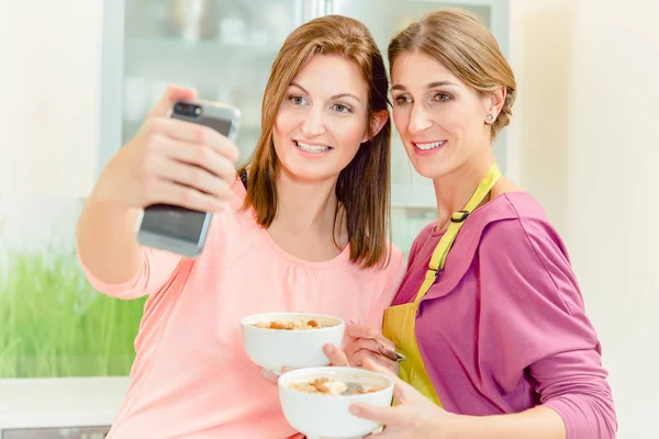 Two female friends holding bowl of oatmeal taking selfie — Stock Photo, Image