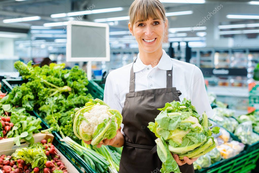 Shop assistant woman in supermarket showing the fresh produce
