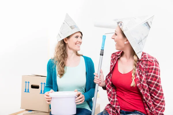 Amigos do sexo feminino usando chapéu de papel segurando balde de pintura e rolo — Fotografia de Stock