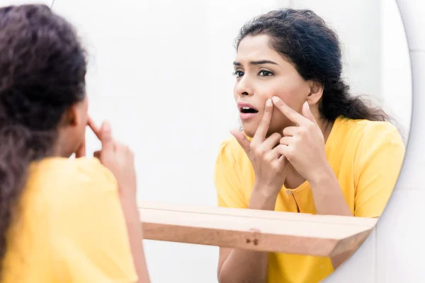 Woman looking in mirror squeezing pimple — Stok fotoğraf