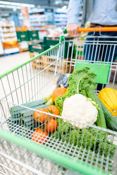 Hombre de compras en el supermercado empujando su carro con verduras — Foto de Stock