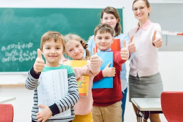 Uczniowie i nauczyciel pokazuje kciuki up w szkole, zabawy — Zdjęcie stockowe