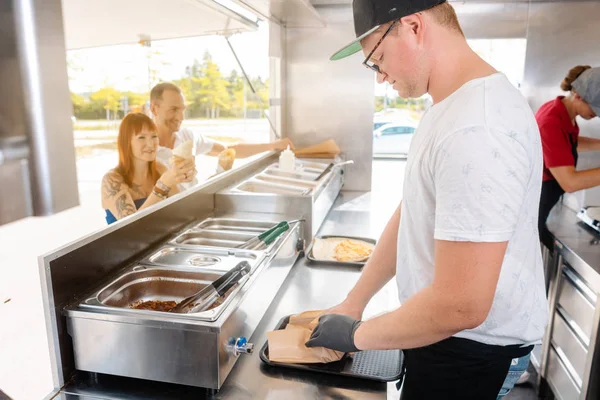 Young chefs in a food truck preparing food for their waiting customers — Stock Photo, Image