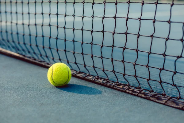Close-up de uma bola amarela fluorescente na frente da rede de um campo de ténis — Fotografia de Stock