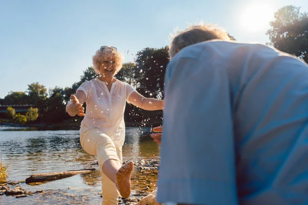 Pareja mayor divertida jugando con agua en el río en un día soleado de verano — Foto de Stock