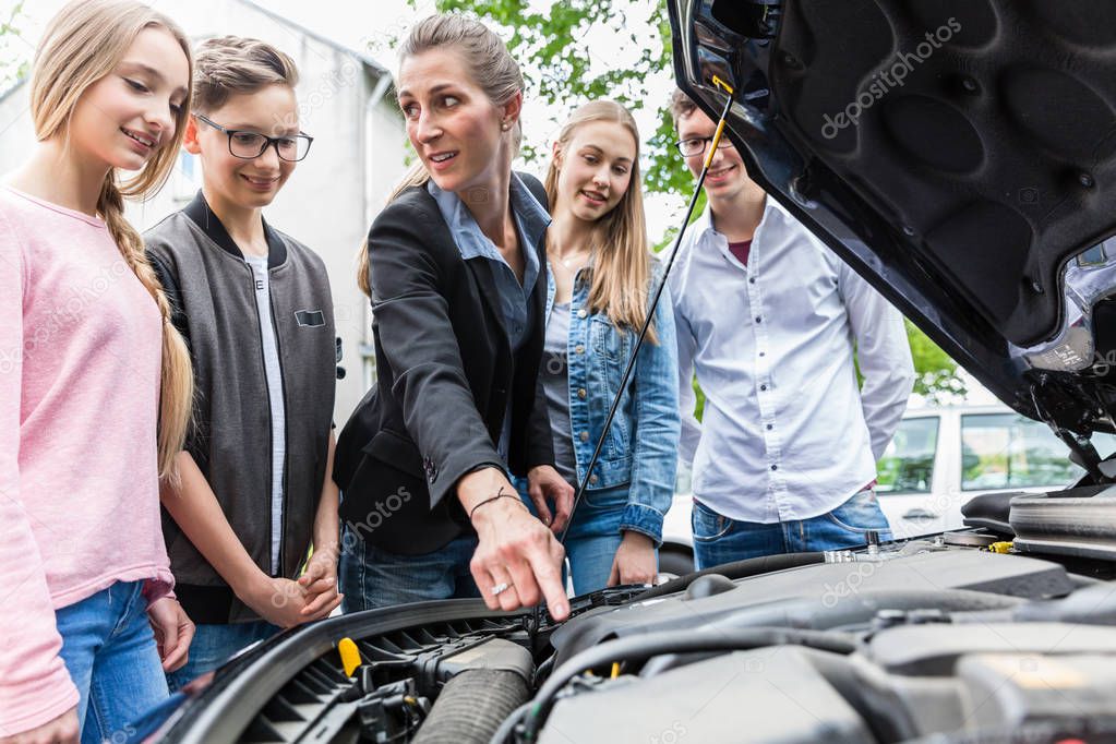 Driving teacher showing class the engine of car