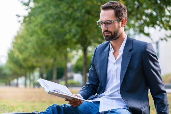 Серьезный бизнесмен читает книгу в парке — стоковое фото