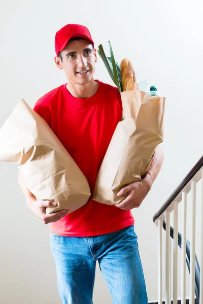 Doručovatel nesoucí dvě nákupní tašky s potravinami s jídlem — Stock fotografie