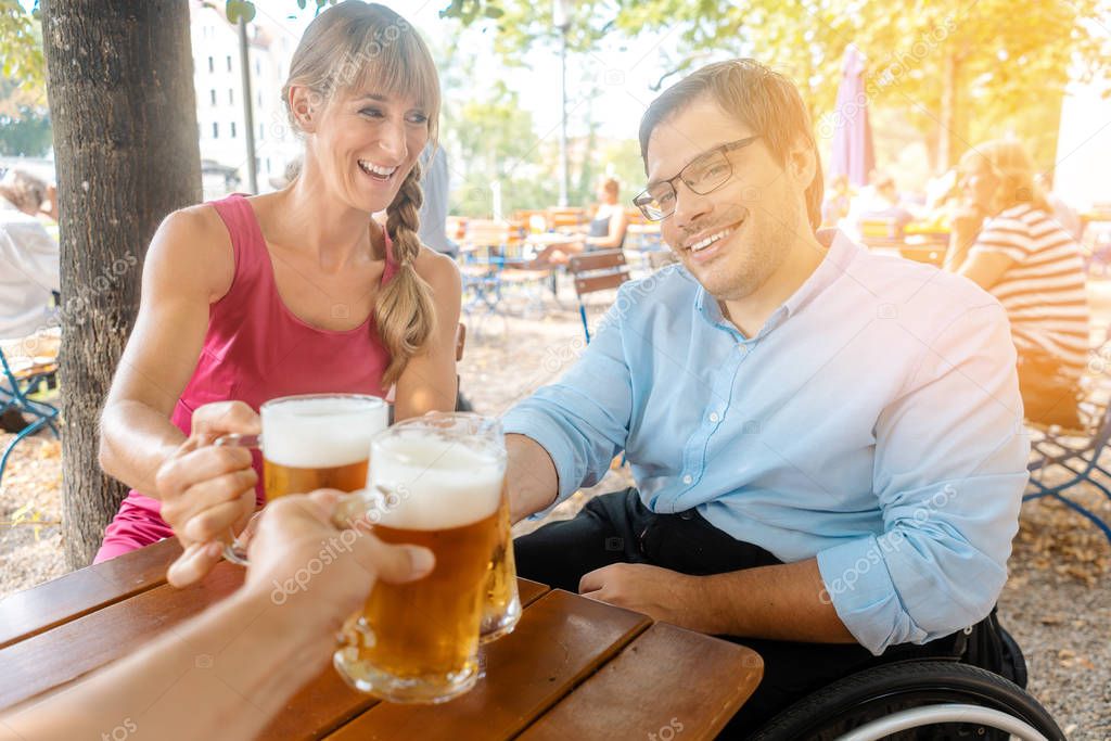 Friends in beer garden drinking, one man is in a wheelchair 