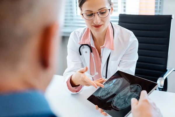 Обеспокоенный врач показывает рентген пациенту — стоковое фото