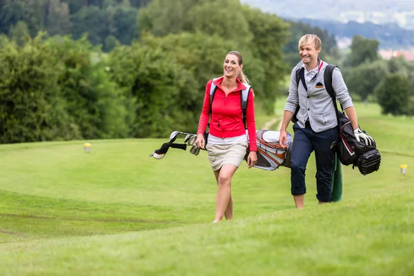 Jogadores de golfe sorridentes carregando seus sacos de clube — Fotografia de Stock