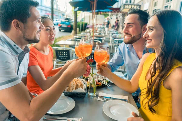 Zwei glückliche junge Paare stoßen beim gemeinsamen Sitzen im Restaurant an — Stockfoto