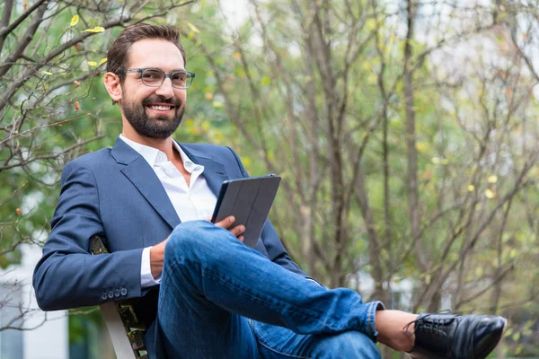 Молодой бизнесмен сидит на скамейке с цифровым планшетом — стоковое фото