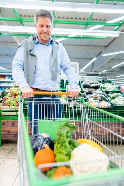 ショッピング スーパー野菜と彼のトロリーを押す男 — ストック写真