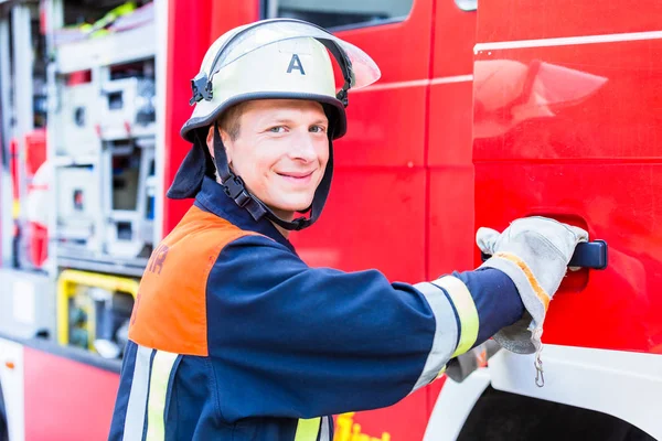 Fire fighter getting on fire engine — Stock Photo, Image