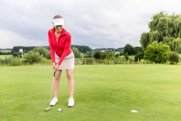 Női golfer elhelyezés golyó lyukba — Stock Fotó