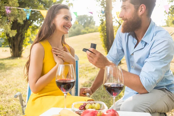 Мужчина показывает красивой девушке обручальное кольцо во время романтического пикника — стоковое фото