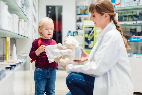 Mulher farmacêutica com cliente criança e seu brinquedo de pelúcia — Fotografia de Stock