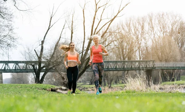 Senior and young woman running as sport on a meadow in spring — Stock Photo, Image