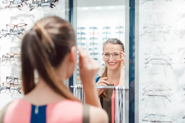 Giovane donna che prova occhiali alla moda nel negozio di optometrista — Foto Stock