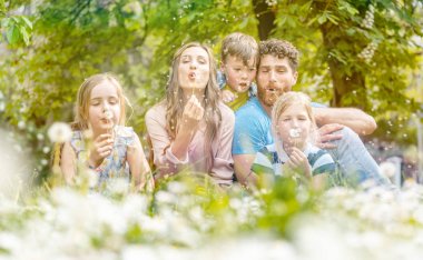 Karahindiba çiçek üfleme bir çayır üzerinde oturan beş kişilik aile