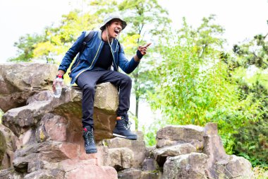 Kaya üzerinde oturan genç adam gülüyor.