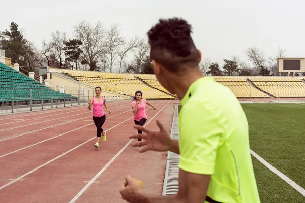 Spor zemininde iki kadın koşucuya bakan adam — Stok fotoğraf