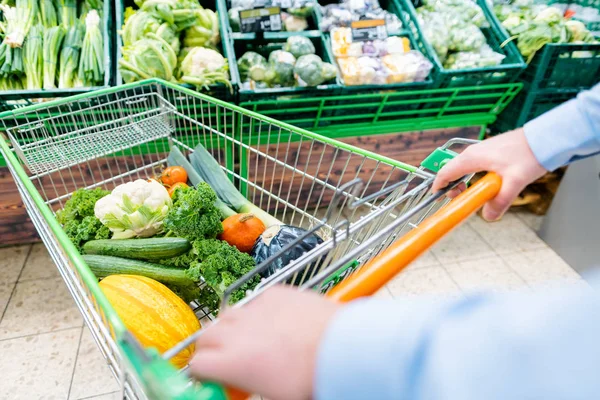 Mann, der im Supermarkt einkauft, schiebt seinen Einkaufswagen mit Gemüse — Stockfoto
