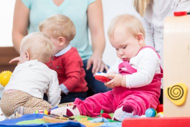 Üç mutlu anne, bebeklerini güvenli çok renkli oyuncaklarla oynarken izliyor
