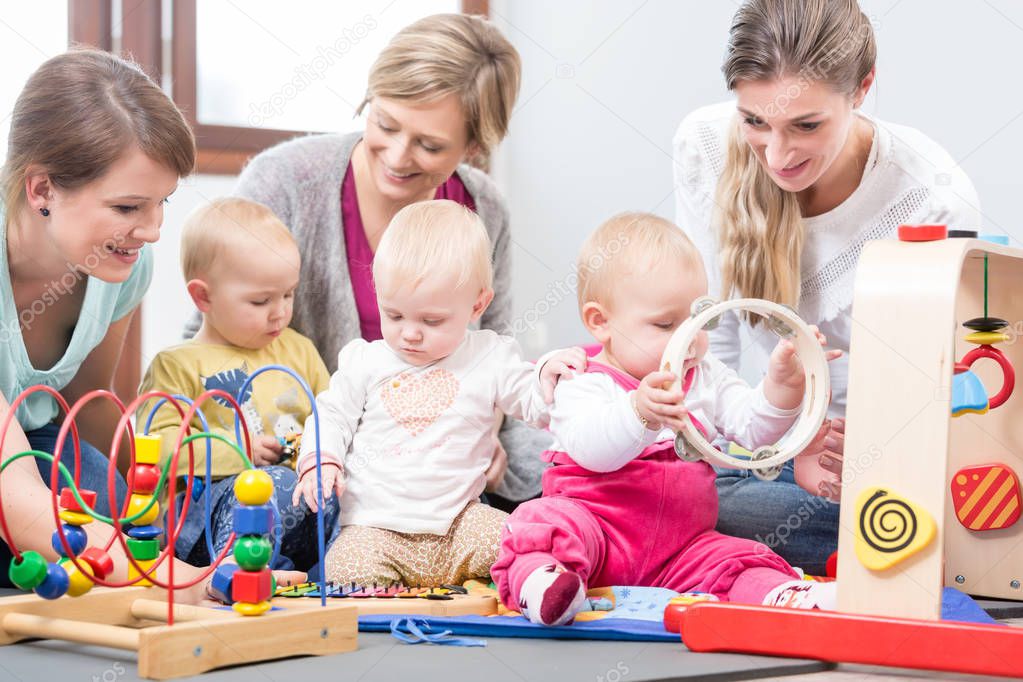 Three happy mothers watching their babies playing with safe multicolored toys
