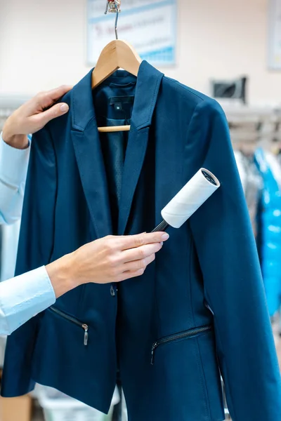 Vrouw in de stomerij winkel gebruikt pluisrol om een jas schoon te maken — Stockfoto