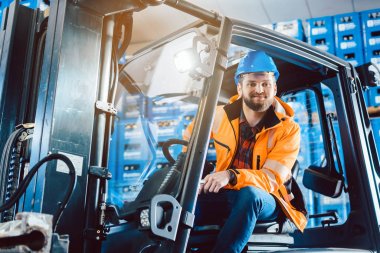 Depoda çalışan bir işçi forkliftinde oturuyor.