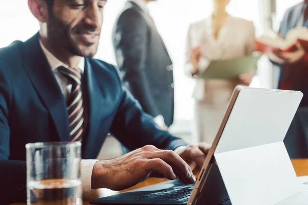 Türkischer Geschäftsmann arbeitet mit Kollegen im Hintergrund am Laptop — Stockfoto