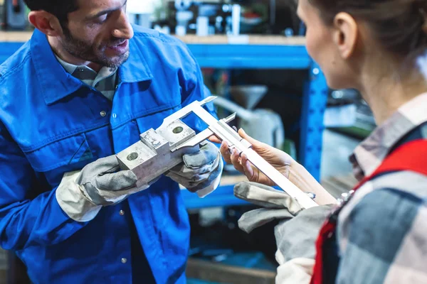 Arbeiterin und Mann prüfen Maße des Metallwerkstücks — Stockfoto