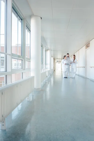 Три врача в больничном коридоре проводят короткую встречу — стоковое фото