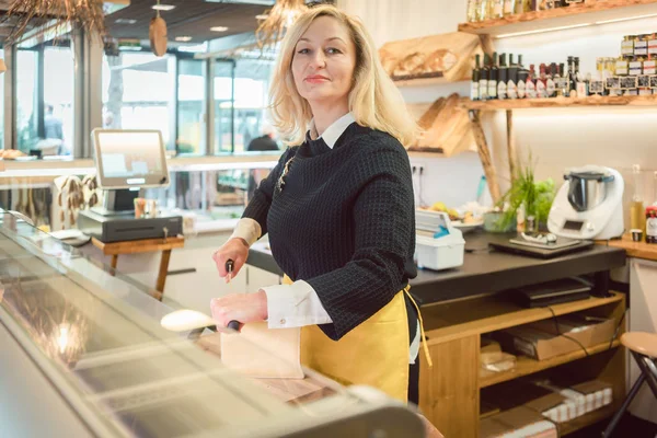 Empleado de tienda en delicatessen cortar queso — Foto de Stock