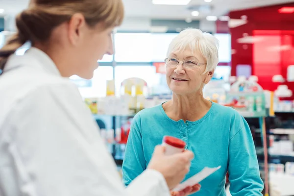 Mujer mayor en farmacia hablando con el químico o farmacéutico — Foto de Stock