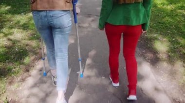 Parkta iki arkadaş, biri kırık bacaklı ve koltuk değneği.