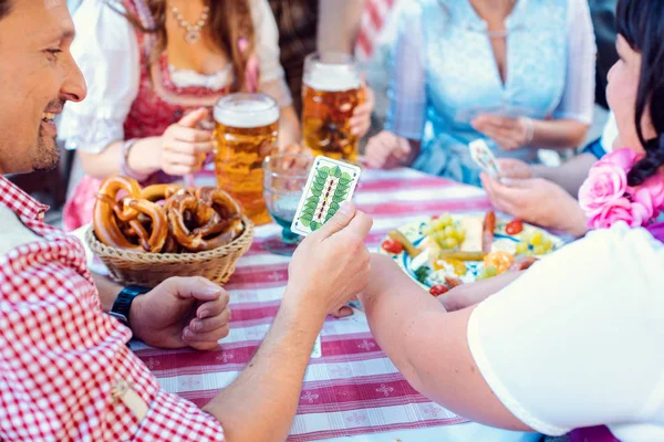 Vrienden in Beierse biertuin spelen traditionele kaartspel — Stockfoto
