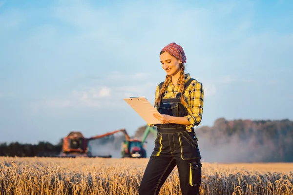 Mulher agricultor com prancheta no campo, colheita acontecendo — Fotografia de Stock