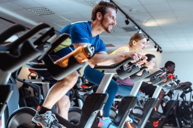 Beyaz adam ve arkadaşları spor salonunda fitness bisikleti üzerinde
