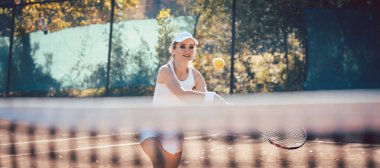 Tenis kortunda top taşıyan bir kadın.