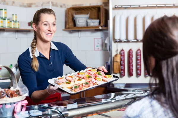 Sales woman in butcher shop offering finger food — Stock Photo, Image